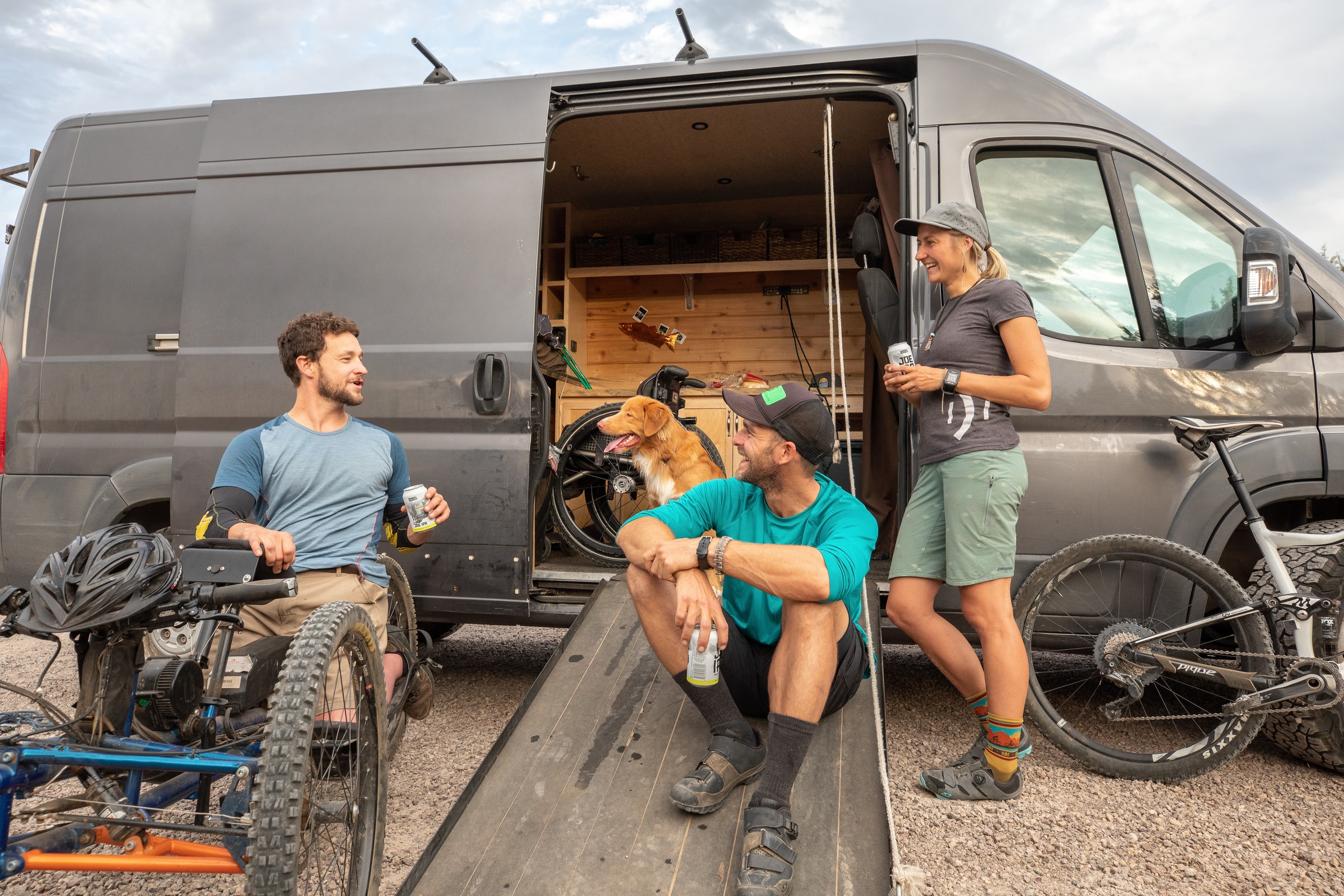 3 friends sitting outside their van with bikes, bears and their dog. One gentleman is in an adapted wheelchair/bike