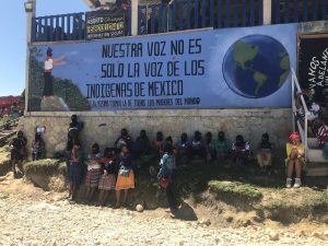 International summit for women in the struggle called by the Zapatistas – Zapatista women hide from the sun under a mural which reads “Our voice is not only the voice of the indigenous women of Mexico, it is also the voice of women of the world”