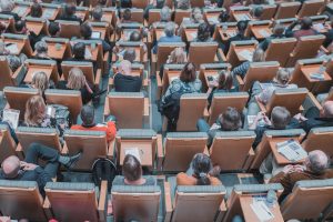 Image taken from above of many students sitting in a university lecture hall.