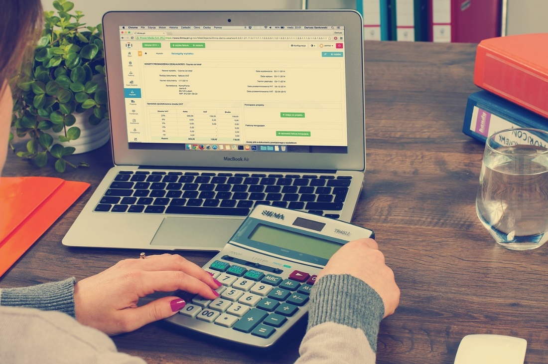 A person operating a laptop and calculator