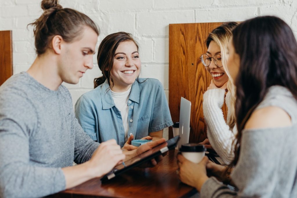 Several people meeting at a table. They are all wearing form fitting clothing with subdued colour tones.