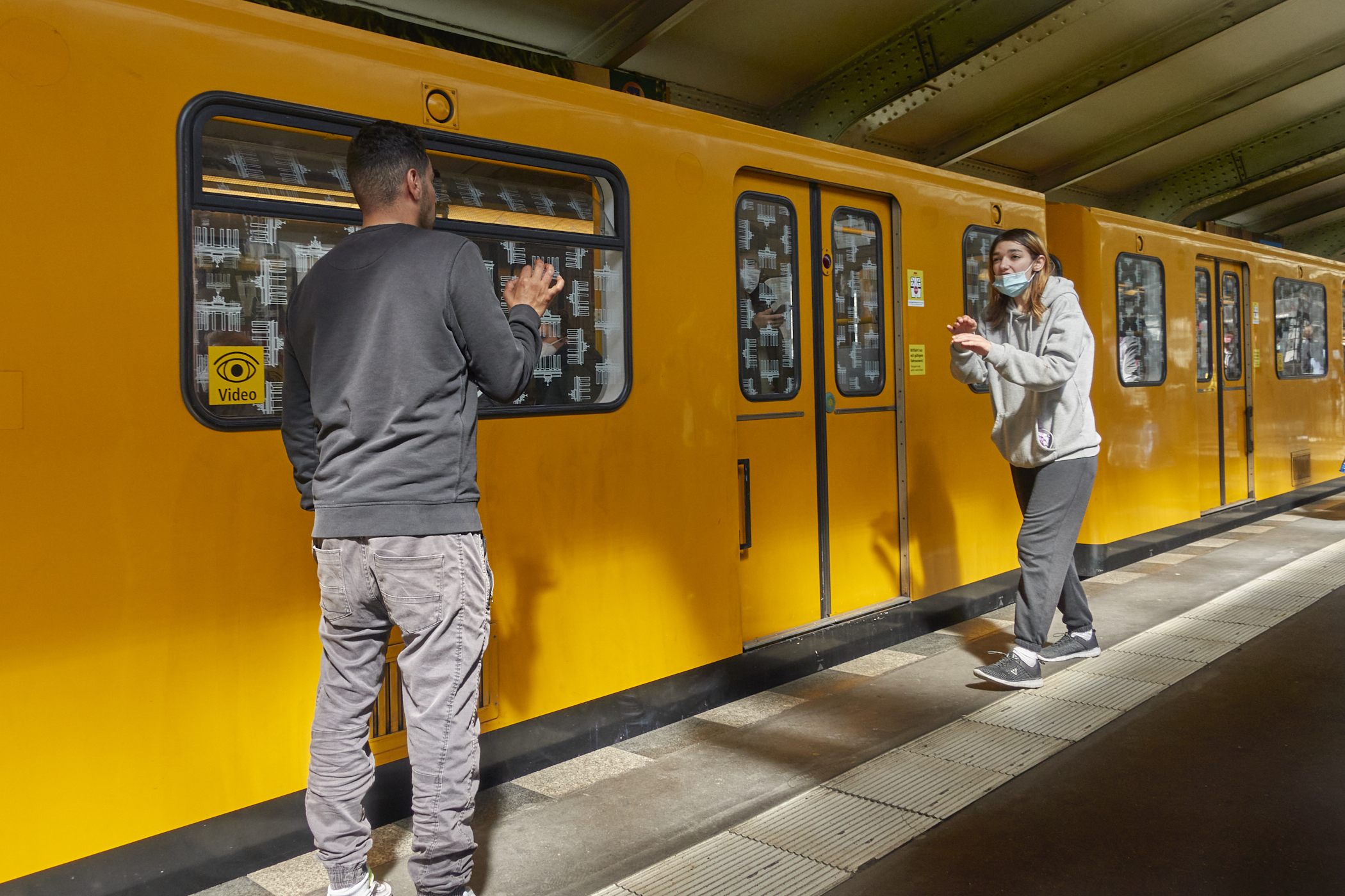 Figure 1 depicts two people standing on a train platform, facing each other. A train is behind them. Each person is gesturing with their hands to convey meaning to the other.