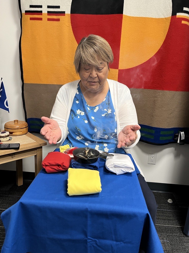 Figure 3 depicts Lynn Lush, the Indigenous Knowledge Keeper at NorQuest College, practising smudging. Lynn is sitting in front of a blanket with a medicine wheel on it. She has burning sage for smudging, in addition to a feather and fabric in the colours of the medicine wheel. She sits with her palms up and her eyes closed.