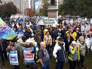 Close up on a group of protester holding banners and sandwich board signs. They are at Queen's Park to show support for striking Ontario faculty.