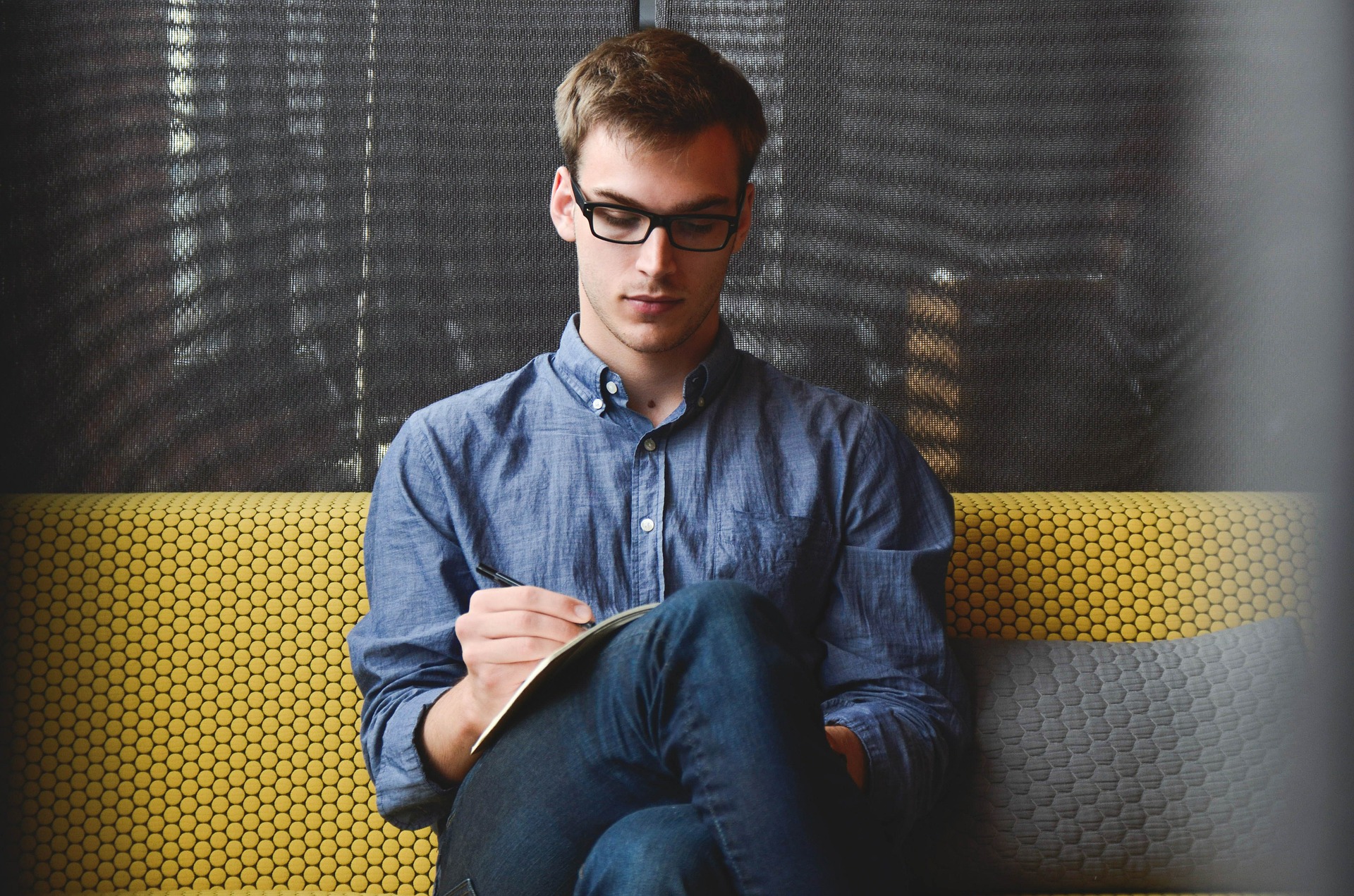 Sven wearing glasses, sitting on a couch and writing in his notebook