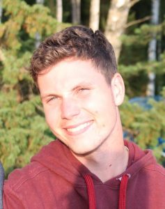 young man with short light brown hair smiling and wearing a read hoodie