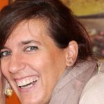 a young woman with long dark brown hair smiling and wearing earrings