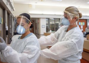 two health care professionals putting on PPE