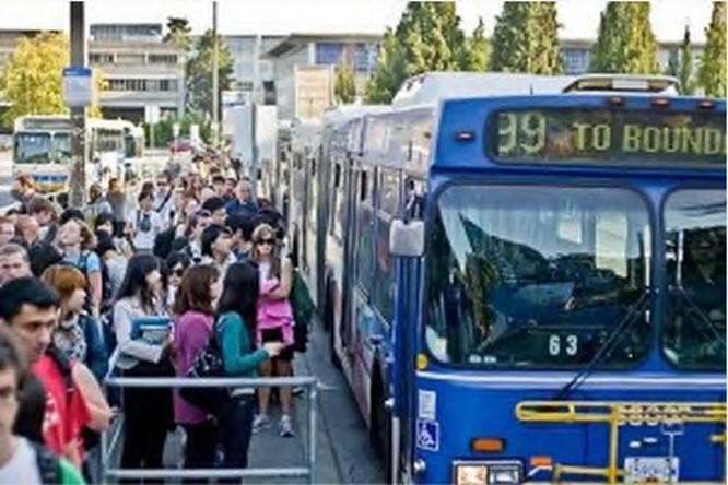 People waiting for a bus at a crowded bus loop at a UBC campus.