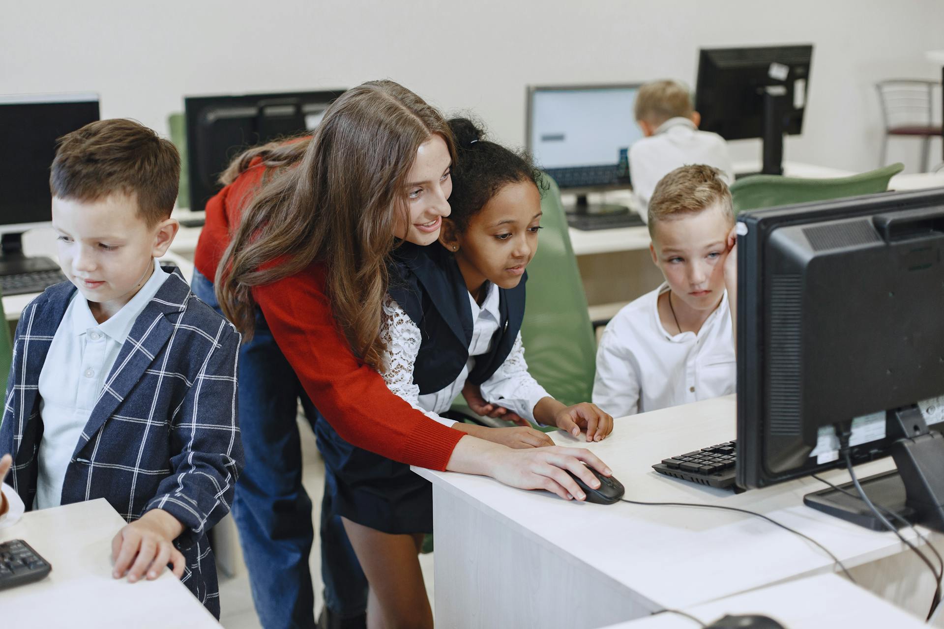A teacher showing two students how to do something at a computer in a computer lab.
