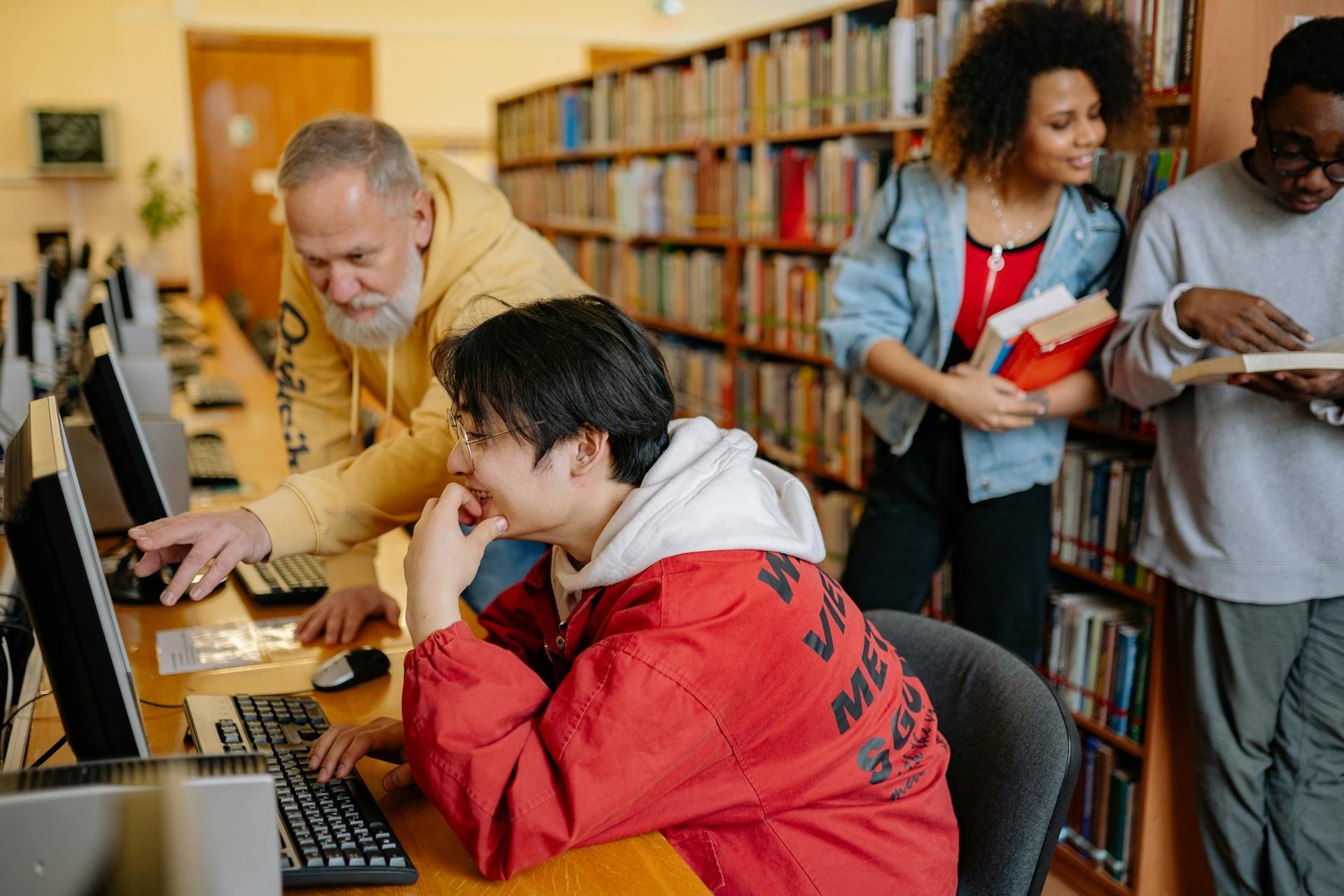 A teacher helping a student who is working on a computer in the library.