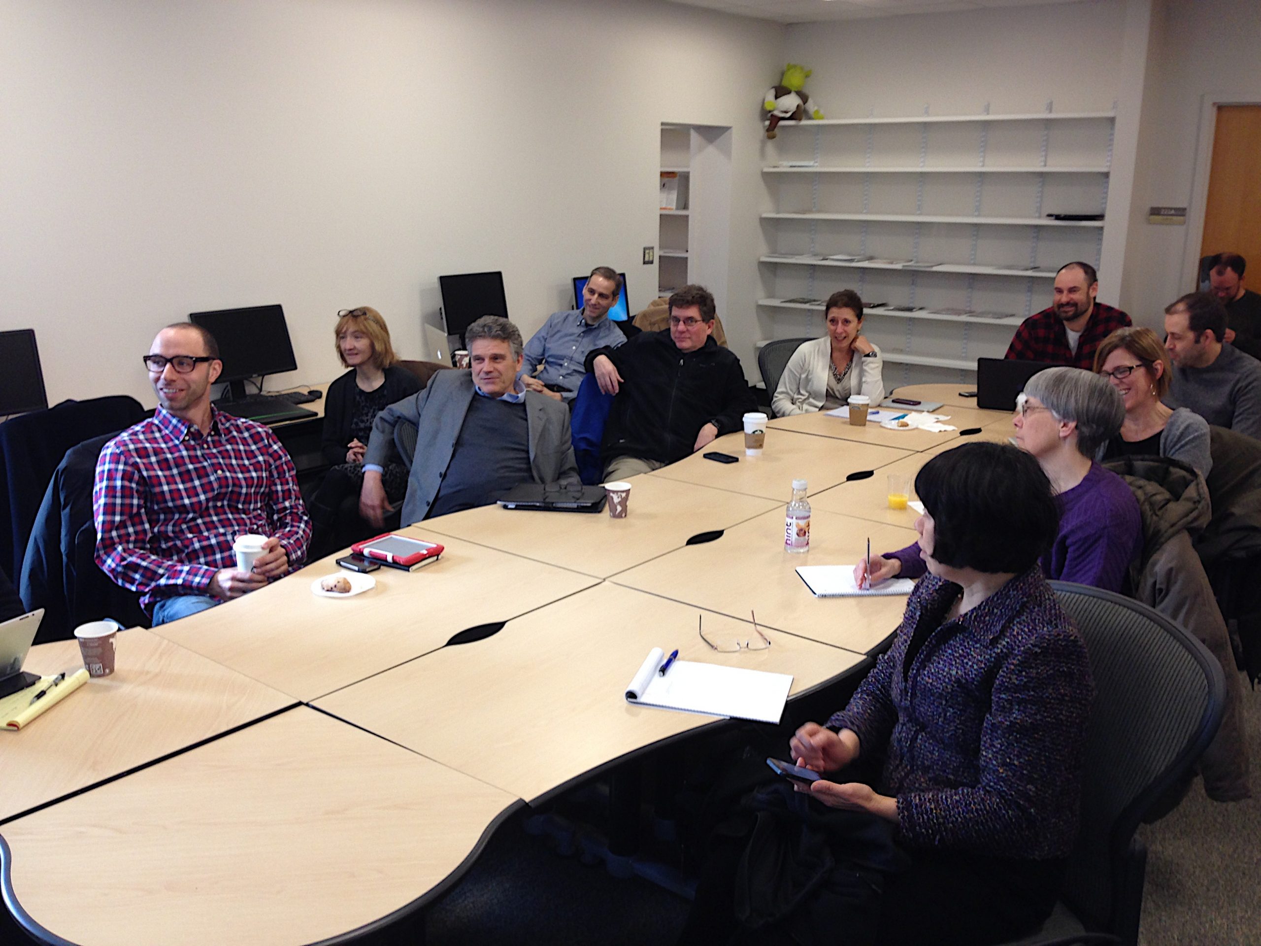 Descriptive image showing approximately 12 individuals seated at a conference table; they are smiling and engaged, giving their full attention to the speaker.