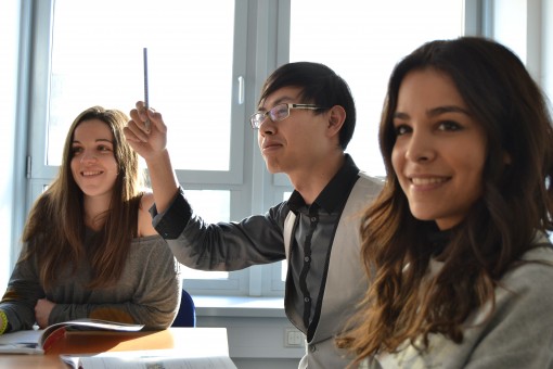 Descriptive image showing 3 young professionals seated at a table, smiling. One person is holding his pencil in the air, as if he is about to ask a question.