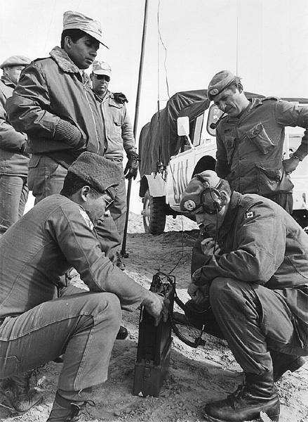 Descriptive image showing a group of four men in military uniforms, circa 1974; one is listening to a radio transmission with a headset.