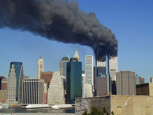 A photograph shows the World Trade Center buildings, shortly after two planes were flown into them on the morning of September 11, 2001. Thick, black clouds of smoke stream from both buildings.