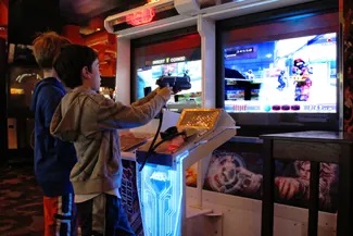 A photograph shows two children playing a video game and pointing a gun-like object toward a screen.